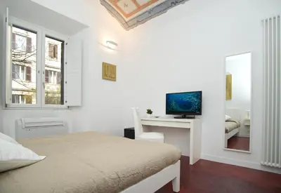 a white bedroom with a bed and a desk with a television at Vatican Charme in Rome