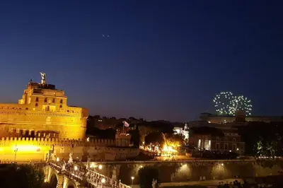a lit up city at night with a bridge and fireworks at La Torre di Castel Sant'Angelo in Rome