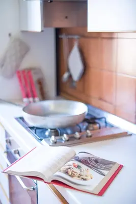 an open book on a kitchen counter with a pan on the stove at ROMA your home in trastevere e gianicolo in Rome