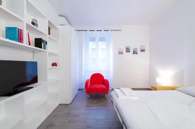a white bedroom with a red chair and a tv at Casa Riboty in Rome