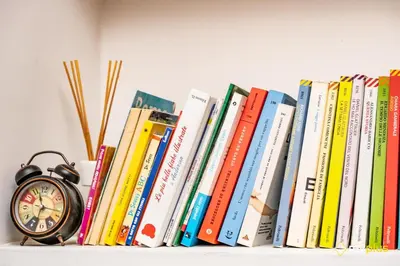 a row of books on a shelf with an alarm clock at Mecenate Apartment Fori Imperiali in Rome