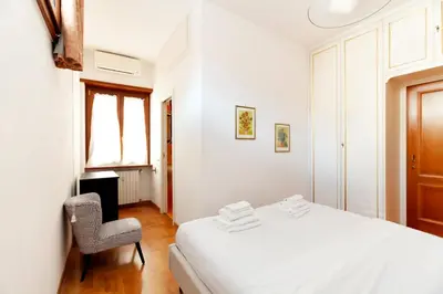 a white bedroom with a bed and a chair at CAVALLEGGERI HOUSE in Rome