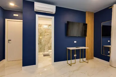 a blue bathroom with a toilet and a tv on the wall at NAIF Suites in Rome
