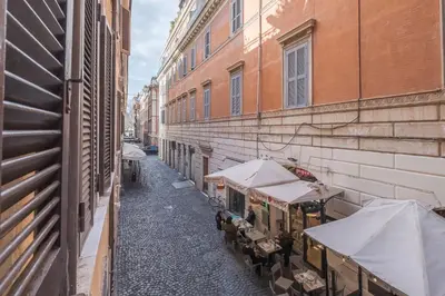an alley with tables and umbrellas next to buildings at Piazza del Popolo - The Heart of Rome in Rome