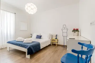 a white bedroom with a bed and a blue chair at True Colors Vatican Home in Rome