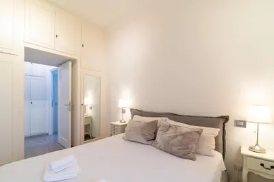 a white bedroom with a white bed with two lamps at Ponte Milvio Holiday Home in Rome