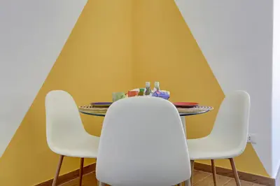 a table with four white chairs and a yellow wall at Furio Camillo Studio - Metro A - Netflix in Rome