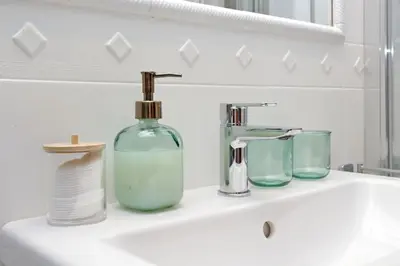 a bathroom sink with a glass bottle and two glasses at La Petite Urbana Apartment in Rome