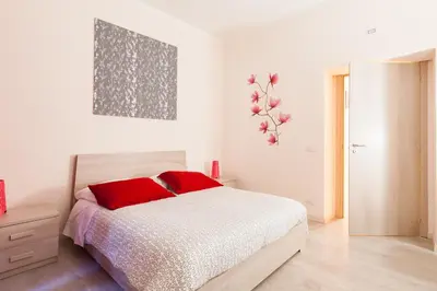 a white bedroom with a bed with two red pillows at San Giovanni Rooms Roma in Rome
