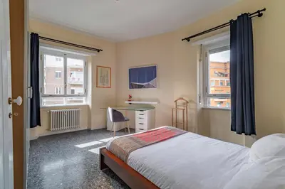 a bedroom with a bed and a desk and two windows at Roma 1950 - Bright apartment in octagonal tower in Rome