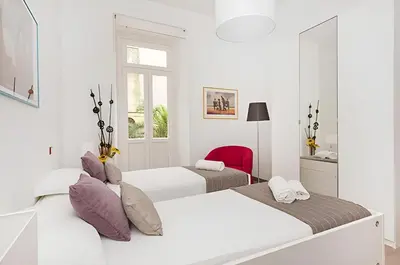 a white bedroom with two beds and a red chair at Ungaretti Vatican Apartment in Rome