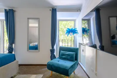a blue chair in a living room with windows at Historic Center - Navona Luxe Haven - Elevator, Soundproof & Netflix in Rome