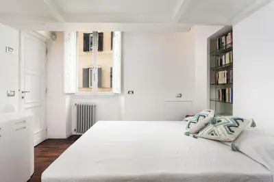 a white bedroom with a large bed and a book shelf at Your nest with wooden ceilings in Monti in Rome