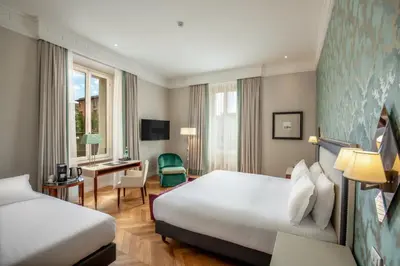 a hotel room with two beds and a desk at Rose Garden Palace Roma by OMNIA hotels in Rome