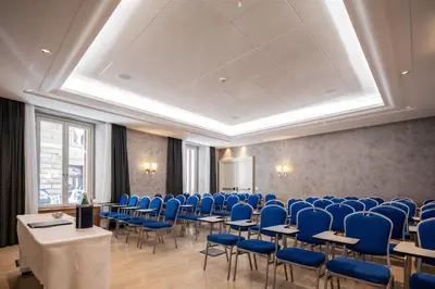 a conference room with blue chairs and tables and a screen at Rose Garden Palace Roma by OMNIA hotels in Rome