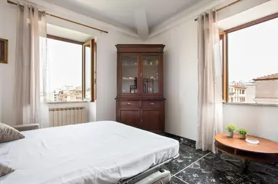 a bedroom with a bed and a table and two windows at Paramount Penthouse in Rome