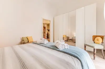 a white bedroom with a large bed and a chair at Wonderful Garden at Colosseo in Rome
