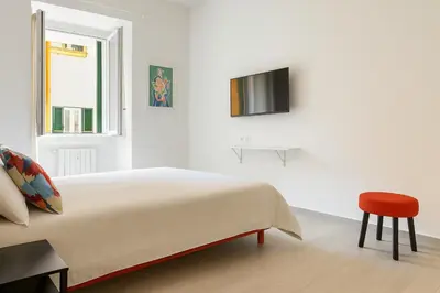 a white bedroom with a bed and a red stool at Ospiti di Jole al Pigneto in Rome