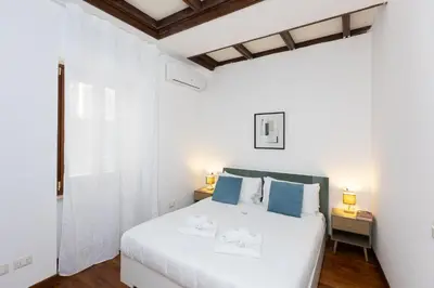 a white bedroom with a large white bed with blue pillows at Vicolo Trevi Apartment by Rental in Rome in Rome