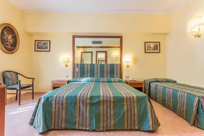 a hotel room with two beds and a chair at Raeli Hotel Noto in Rome