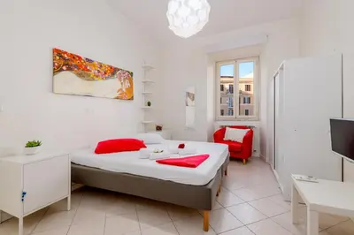 a white bedroom with a bed and a red chair at Domus Aurea3 flat a stone's throw from Colosseum in Rome