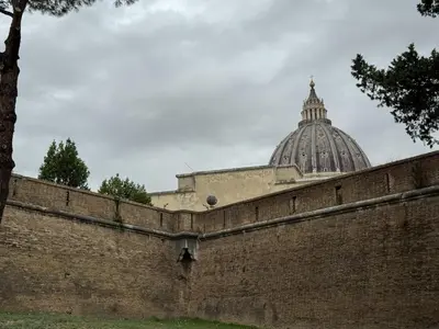 a building with a dome behind a brick wall at San Pietro Apartment Vatican 5 min Walk in Rome