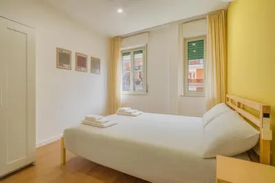 a bedroom with a bed with white sheets and two windows at Pigneto Mood Comfort nel Cuore Creativo di Roma in Rome