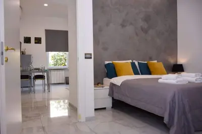 a bedroom with a bed with colorful pillows and a kitchen at Rampa Brancaleone Apartment in Rome
