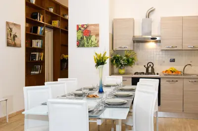 a dining room table with white chairs and a kitchen at House Gregorio in Rome