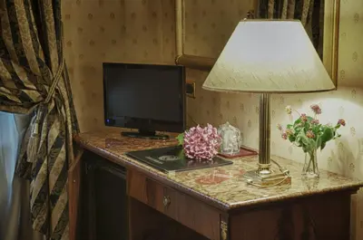 a lamp on a desk with a television and flowers at Hotel Cilicia in Rome