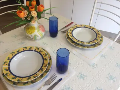 a table with plates and blue glasses and a vase with flowers at Lovely Little Apartment in Via Aurelia in Rome