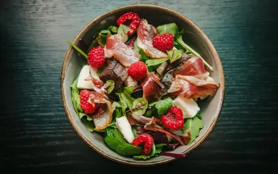 a bowl of salad with strawberries on a table at Tree Charme Parliament Boutique Hotel in Rome
