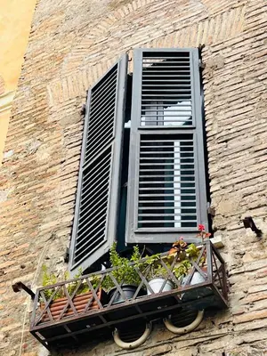 a window on a brick building with a balcony with plants at Torre Tolomei Trastevere in Rome