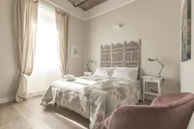 a white bedroom with a bed and a chair at Casa di Ele in Rome