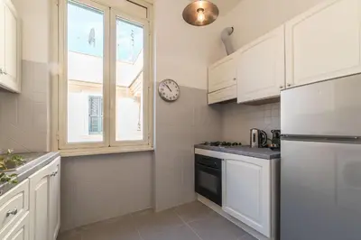 a kitchen with white cabinets and a clock on the wall at Lively Roma Trastevere renovated apartment - FromHometoRome in Rome