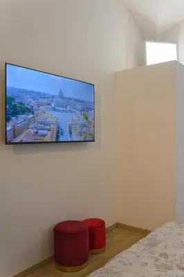 a bedroom with two red stools and a tv on the wall at Domus Vatican Museum in Rome