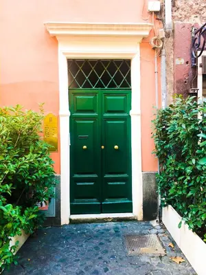 a green door on a pink building with bushes at Romantico appartamento a Trastevere in Rome