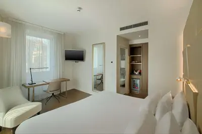 a white bedroom with a white bed and a desk at NH Collection Roma Centro in Rome