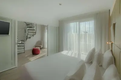 a white bedroom with a bed and a large window at NH Collection Roma Centro in Rome