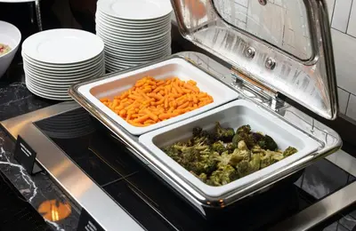 a tray of carrots and broccoli on a stove at NYX Hotel Rome by Leonardo Hotels in Rome