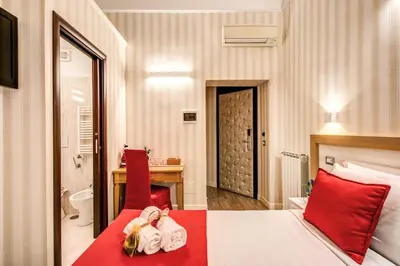 a hotel room with a bed with red pillows and a bathroom at Auditorium Mecenate in Rome