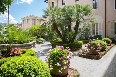 a garden with flowers and palm trees and a building at Donna Camilla Savelli - VRetreats in Rome