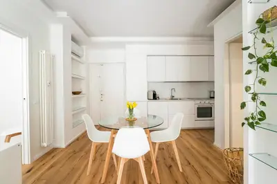 a white kitchen with a glass table and white chairs at Trastevere Boutique Apartment in Rome
