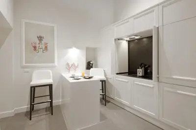 a white kitchen with white cabinets and white stools at Carthusia Suites Roma in Rome